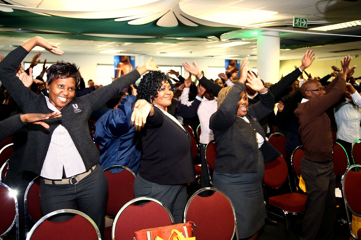 A room of delegates laughing with arms raised during a Laughter Coaching session