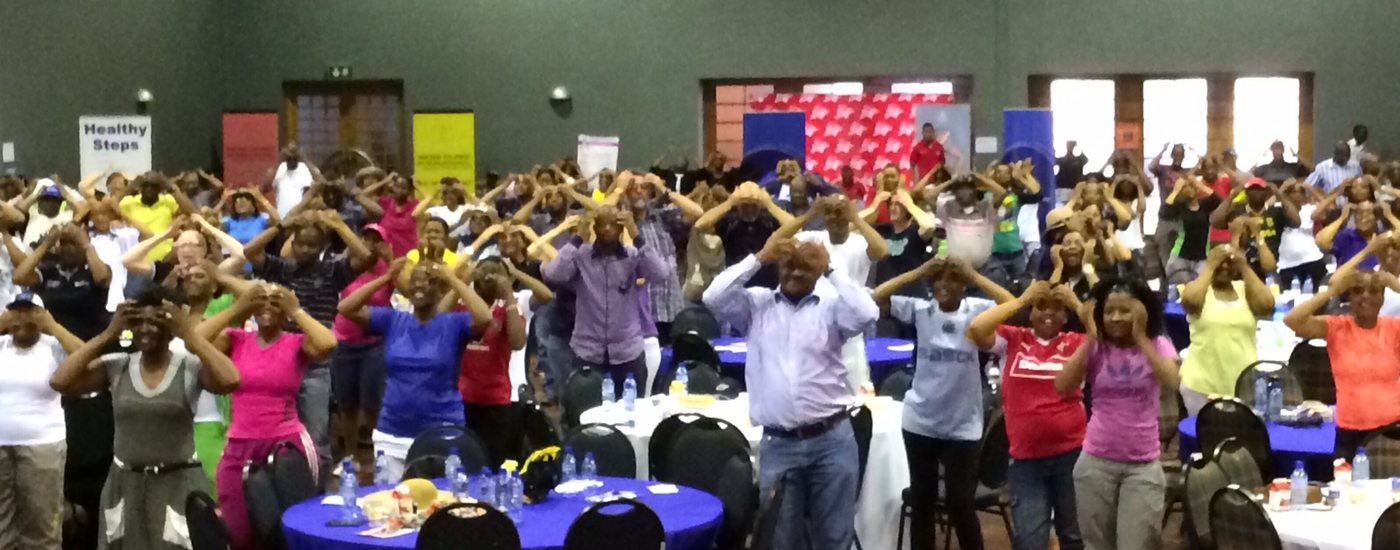 A wide conference hall of employees laughing with their arms raised